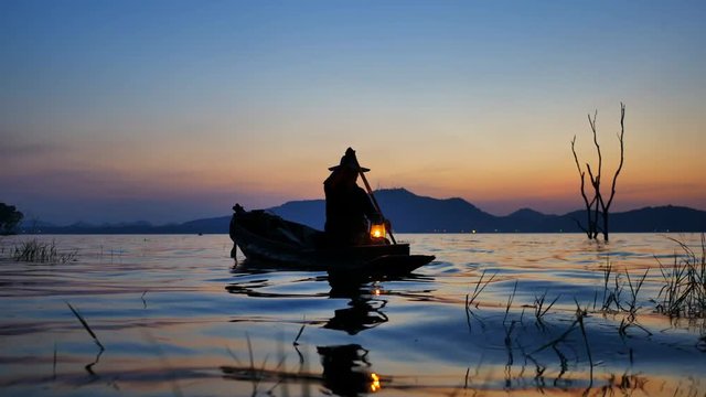 Silhouette scene of Fisherman on boat fishing with a fishnet. He use old traditional fishing equipment for fishing in The lake. Bang Phra Lake - Eastern of Thailand