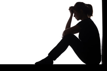 silhouette of a woman sitting on the floor in a corner on a white isolated background, a sad girl...