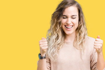 Beautiful young blonde woman wearing sweatershirt over isolated background excited for success with arms raised celebrating victory smiling. Winner concept.