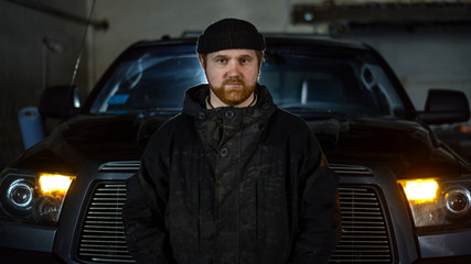 Portrait of a serious man with a beard in uniform near a pickup truck