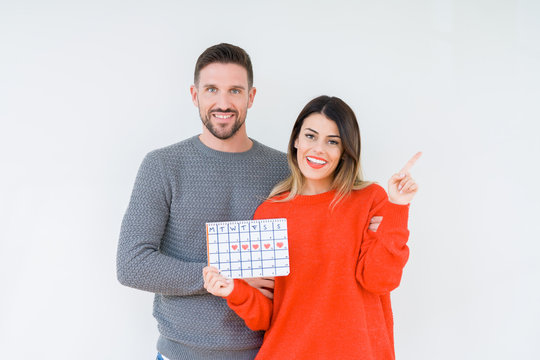Young couple holding ovulation calendar over isolated background very happy pointing with hand and finger to the side