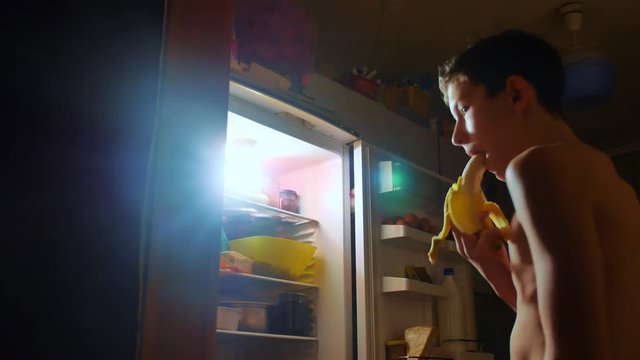 young boy eats hunger and gluttony from the refrigerator at night. teen boy looks into the fridge at night. gluttony overweight lifestyle overeating concept