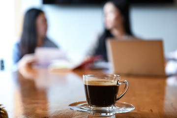 Coffee cup on deak in the meeting room. Blurred background workers are sitting.