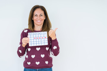 Middle age woman holding menstruation calendar over isolated background happy with big smile doing ok sign, thumb up with fingers, excellent sign