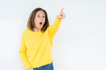Beautiful middle age woman wearing yellow sweater over isolated background Pointing with finger surprised ahead, open mouth amazed expression, something in front