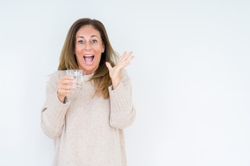 Middle age woman drinking glass of water isolated background very happy and excited, winner expression celebrating victory screaming with big smile and raised hands