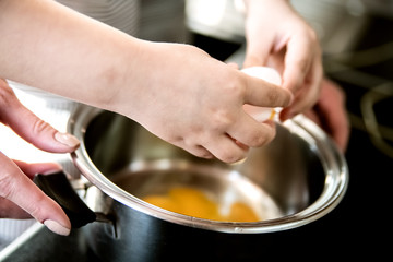 A child helps mom cook breakfast and breaks eggs into a saucepan.
