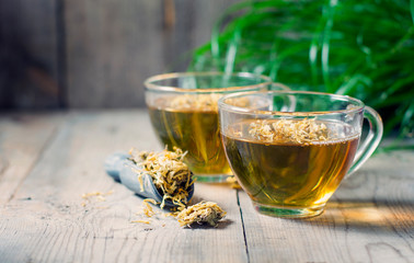 Herbal tea in a transparent glass mug with calendula flowers on a wooden background. Phytotea