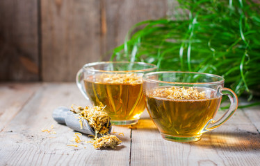 Herbal tea in a transparent glass mug with calendula flowers on a wooden background. Phytotea