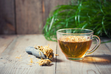 Herbal tea in a transparent glass mug with calendula flowers on a wooden background. Phytotea