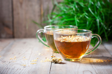 Herbal tea in a transparent glass mug with calendula flowers on a wooden background. Phytotea