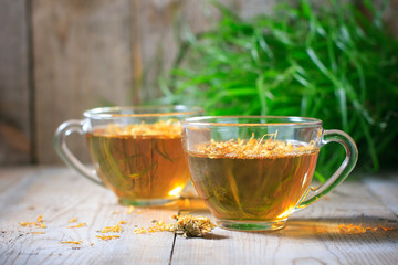 Herbal tea in a transparent glass mug with calendula flowers on a wooden background. Phytotea