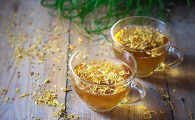 Herbal tea in a transparent glass mug with calendula flowers on a wooden background. Phytotea