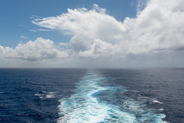 Foam trail in the sea behind the stern of the ship against the horizon and clouds
