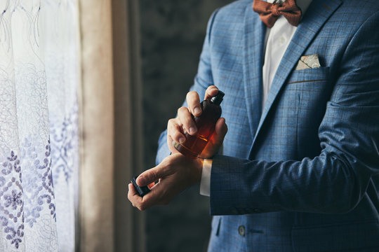 Handsome guy is choosing perfumes, Elegant man in suit using cologne,groom getting ready in the morning before wedding ceremony