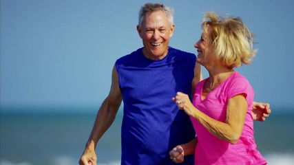 Active retired Caucasian couple enjoying jogging on the ocean beach