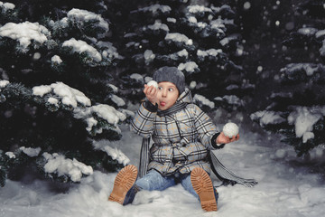 A little girl in winter clothes playing with snow on a snowy meadow surrounded by fir trees. Christmas concept. Studio shot