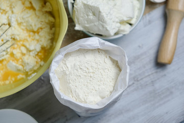 Cooking process of homebaked cottage cheese pie. Raw ingredients in bowl and flour. Table with kitchen objects. Top view flat lay with space for text.