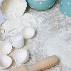 Fototapeta na wymiar Table with ingredients for dough, raw eggs, flour, plate, napkins, rolling pin. Process of preparing pie, kitchen objects, flat lay with light white and blue colors space for text