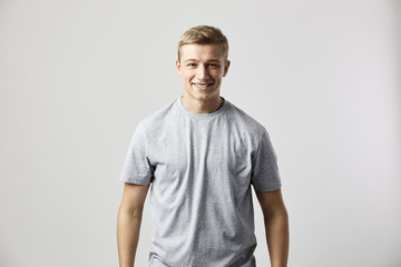 Fototapeta premium Smiling guy dressed in a white t-shirt stands on the white background in the studio