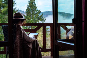 Young woman traveler sits at the terrace with a tablet against beautiful mountain scenery during...