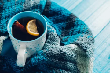 Wall murals Tea A mug of hot tea with cinnamon on a blue background with a scarf