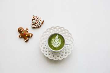 Fresh useful green matcha latte coffee in a beautiful mug on a white background. Nearby lay Christmas gingerbread.