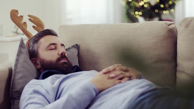 A man with reindeer headband lying on a sofa at Christmas time, sleeping.