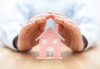 Property insurance. House miniature covered by hands. 