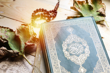 Holy book quran and rosary and leaves on wooden table