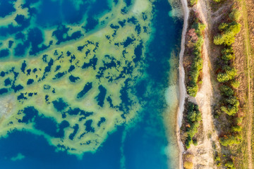 Fototapeta na wymiar Abstract aerial image of a deep blue gravel lake with sandbanks almost reaching the surface of the water.