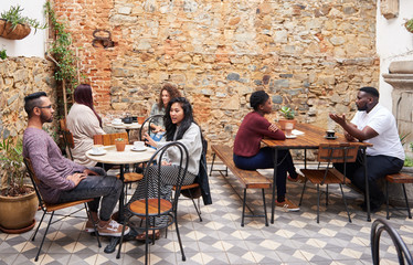 Diverse crowd talking over drinks in a trendy cafe courtyard - obrazy, fototapety, plakaty