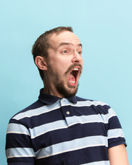 The surprised and astonished young man screaming with open mouth isolated on blue background. concept of shock face emotion