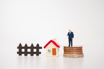 Miniature people, businessman standing on coins with mini house isolated on white background using as business concept