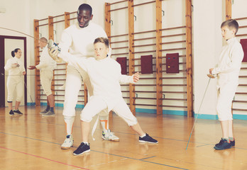 Focused boys fencers attentively listening to professional fencing coach in gym