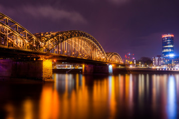 Blick auf die beleuchtete Hohenzollernbrücke, den Köln Triangle, das Hyatt Hotel und den Fluss Rhein in Köln bei Nacht.