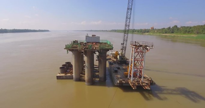 aerial fly towards the bridge foundation and the barge mounted crane in river