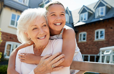 Fototapeta na wymiar Granddaughter Hugging Grandmother On Bench During Visit To Retirement Home