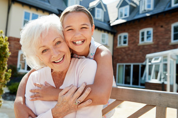 Fototapeta na wymiar Portrait Of Granddaughter Hugging Grandmother On Bench During Visit To Retirement Home