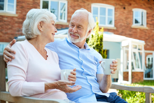 Retired Couple Sitting On Bench With Hot Drink In Assisted Living Facility