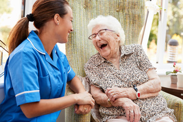 Senior vrouw zittend in een stoel en lachen met verpleegster in bejaardentehuis