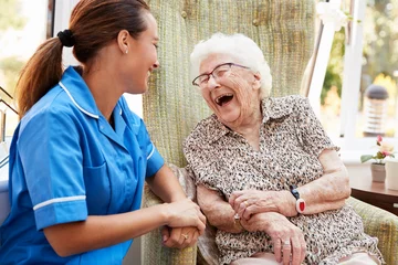Foto auf Acrylglas Pflegezentrum Ältere Frau auf Stuhl sitzend und lachend mit Krankenschwester im Altersheim