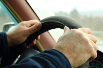 The driver in the car. Men's hands on the steering wheel. Close-up. Background.