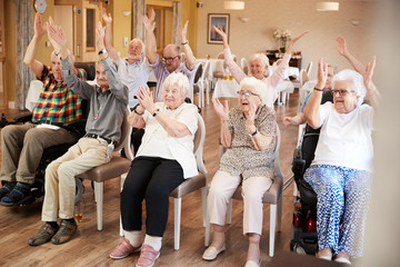 Group Of Seniors Enjoying Fitness Class In Retirement Home - obrazy, fototapety, plakaty