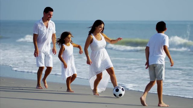 Latin American family playing together on beach holiday with soccer ball