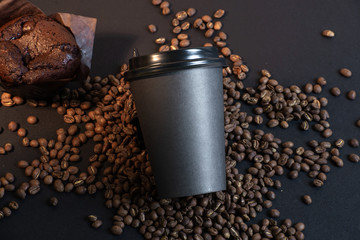 Black coffee cup and muffin in coffee beans on black background.