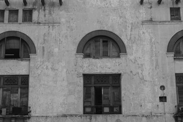Fototapeta na wymiar Old, Spanish style cement building, Havana, Cuba. Arched window frames, broken shutters and doors, chipped and pealing paint. Black and White