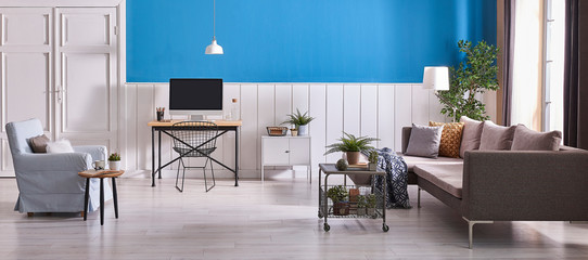 White and blue color wall, wooden desk and desktop, blue armchair and grey decorative sofa. Grey metal coffee table and grey cabinet.