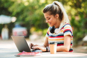 Happy young cute girl student sitting in park using laptop computer.