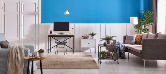 Decorative blue armchair and grey sofa with wooden desk. Desktop white lamp and carpet style. Classic door.